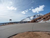 a man is riding his bike down a mountain road with snow and rocks in the background