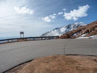 a man is riding his bike down a mountain road with snow and rocks in the background