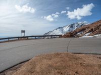 a man is riding his bike down a mountain road with snow and rocks in the background