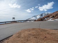 a man is riding his bike down a mountain road with snow and rocks in the background