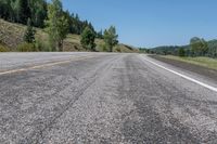 an empty open highway with the woods in the background and blue skies above it is yellow lines