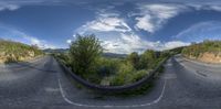 a fish eye view of a road through trees and shrubs, near some hills and water