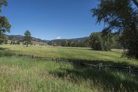 a field that is near the fence of a farm in a rural country setting with mountains behind it