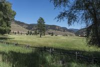 a field that is near the fence of a farm in a rural country setting with mountains behind it