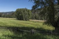 a field that is near the fence of a farm in a rural country setting with mountains behind it