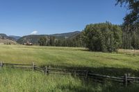 a field that is near the fence of a farm in a rural country setting with mountains behind it