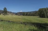 a field that is near the fence of a farm in a rural country setting with mountains behind it