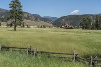 a field that is near the fence of a farm in a rural country setting with mountains behind it