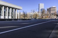 a empty city street in a large city with tall buildings and columns in the background