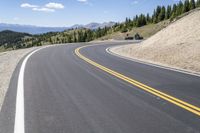 a man riding a motorcycle down a road next to trees on a hill side under a blue sky