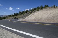 a man riding a motorcycle down a road next to trees on a hill side under a blue sky