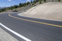 a man riding a motorcycle down a road next to trees on a hill side under a blue sky