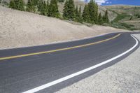 the empty winding road curves into the distance between mountains and trees of the nearby area