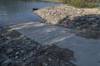 a bench by the water beside the shore with some rocks and logs in it by a concrete wall