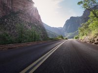 the sun shines brightly on a straight road near a cliff area with trees and a canyon wall