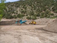 two yellow bulldozers work on sand and gravel in a mountain valley while another one looks at it