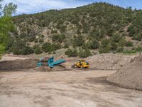 two yellow bulldozers work on sand and gravel in a mountain valley while another one looks at it