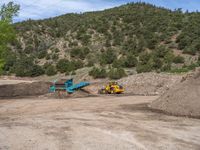 two yellow bulldozers work on sand and gravel in a mountain valley while another one looks at it