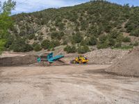 two yellow bulldozers work on sand and gravel in a mountain valley while another one looks at it