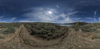 a fisheye view of an old dirt road through the desert with water, grass and bushes