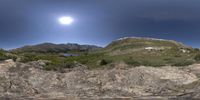 an image of the moon above the mountains in the sky over the water to the right of a river and small green hills