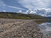 a lake with rocks on the shore and mountains in the background along side it and snow capped hills