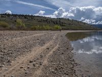 a lake with rocks on the shore and mountains in the background along side it and snow capped hills