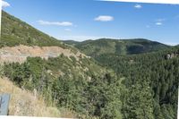 scenic area with steep mountains and pine trees, in the background are rolling hills and valleys