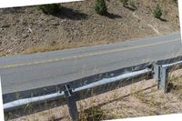 a motorcycle is sitting on the side of a road next to a guardrail as a mountain passes by