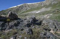 person with a backpack standing on top of a mountain slope covered in rocks and green grass