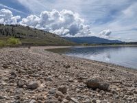 a lake with rocks on the shore and mountains in the background along side it and snow capped hills