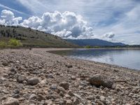 a lake with rocks on the shore and mountains in the background along side it and snow capped hills