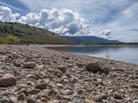 a lake with rocks on the shore and mountains in the background along side it and snow capped hills