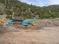 two yellow bulldozers work on sand and gravel in a mountain valley while another one looks at it