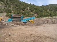 two yellow bulldozers work on sand and gravel in a mountain valley while another one looks at it