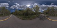 a mirror view on a country road through the woods with cloudy skies above it, and a sun in the distance