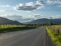 a lone country road is in the countryside area with mountains on both sides and barbed fence between the two sides