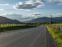 a lone country road is in the countryside area with mountains on both sides and barbed fence between the two sides