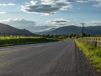 a lone country road is in the countryside area with mountains on both sides and barbed fence between the two sides