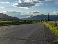 a lone country road is in the countryside area with mountains on both sides and barbed fence between the two sides