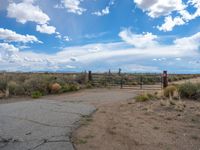 a gate is open at the entrance to the dry desert area near an old horse farm