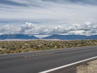 the view of mountains from an empty highway with some clouds over the mountains in the distance