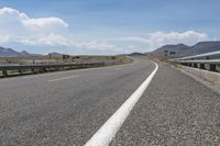 a wide open road with multiple lanes near some mountains and trees with blue sky with white clouds