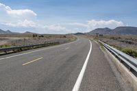 a wide open road with multiple lanes near some mountains and trees with blue sky with white clouds