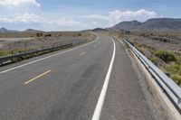 a wide open road with multiple lanes near some mountains and trees with blue sky with white clouds