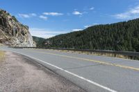 a road with a mountain next to it and a treeline at the top of one side