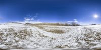 a truck traveling through a dirt covered field in the snow beneath a blue sky with some clouds