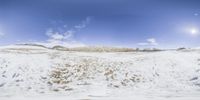 a wide panorama with the sun on the horizon, showing a snowy field and a mountain