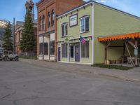 a red fire hydrant sitting in front of an old store window and building next to an open air field