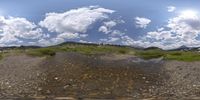 a picture taken in fish - eye lens of water and mountains below the clouds and a small creek